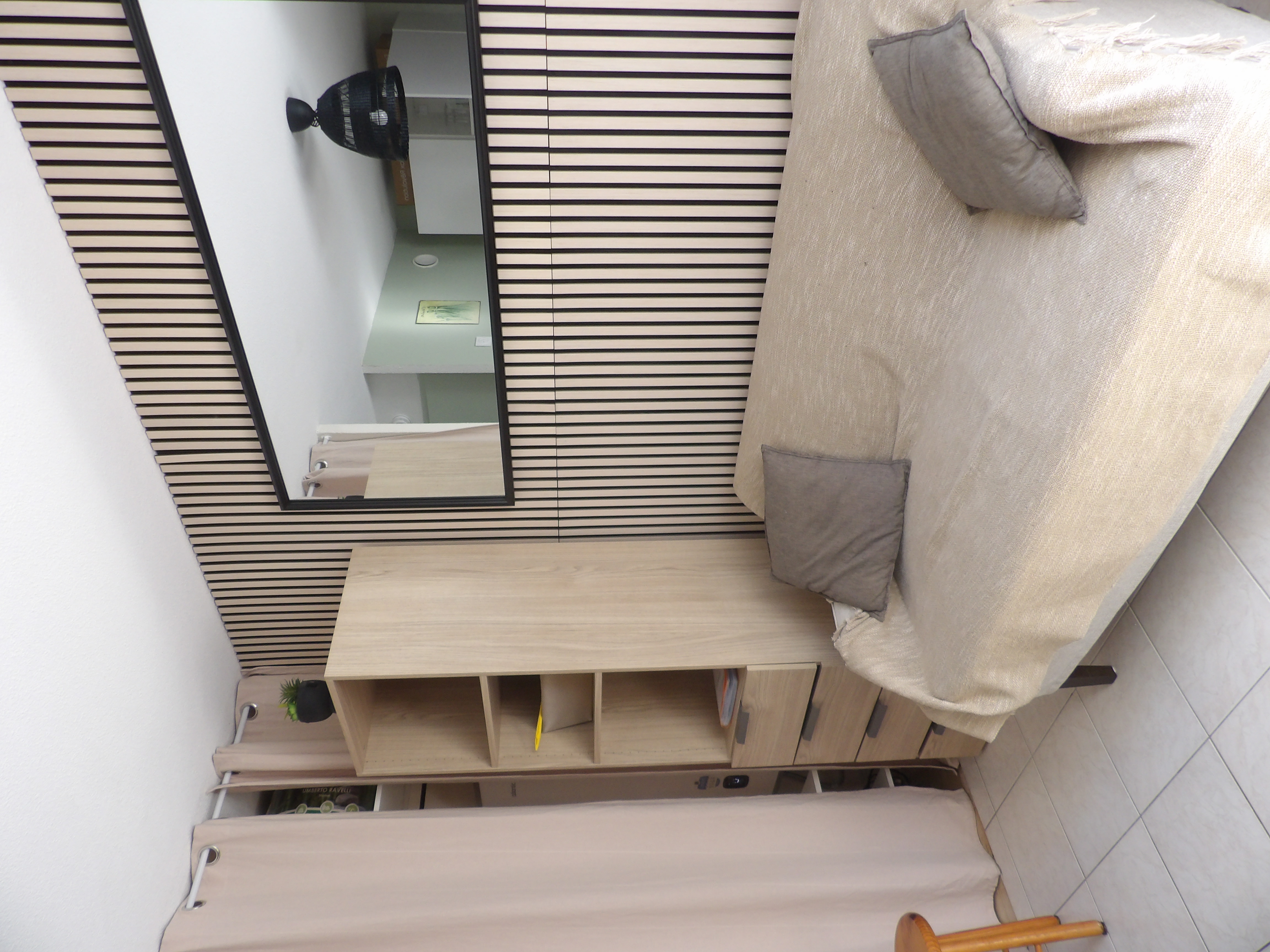 Salon avec canapé beige, coussins, colonne de rangement en bois et grand miroir